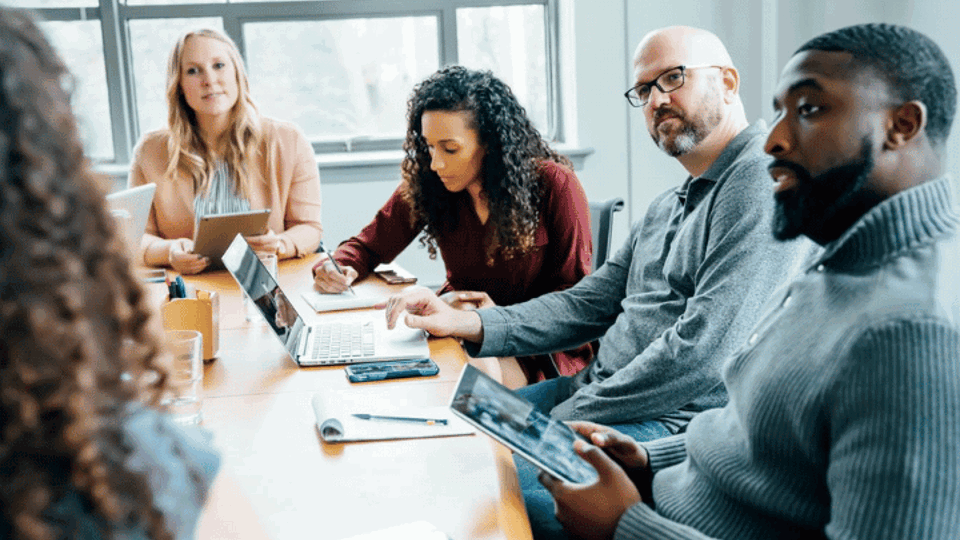 Diverse group of people sitting round a desk in discussion