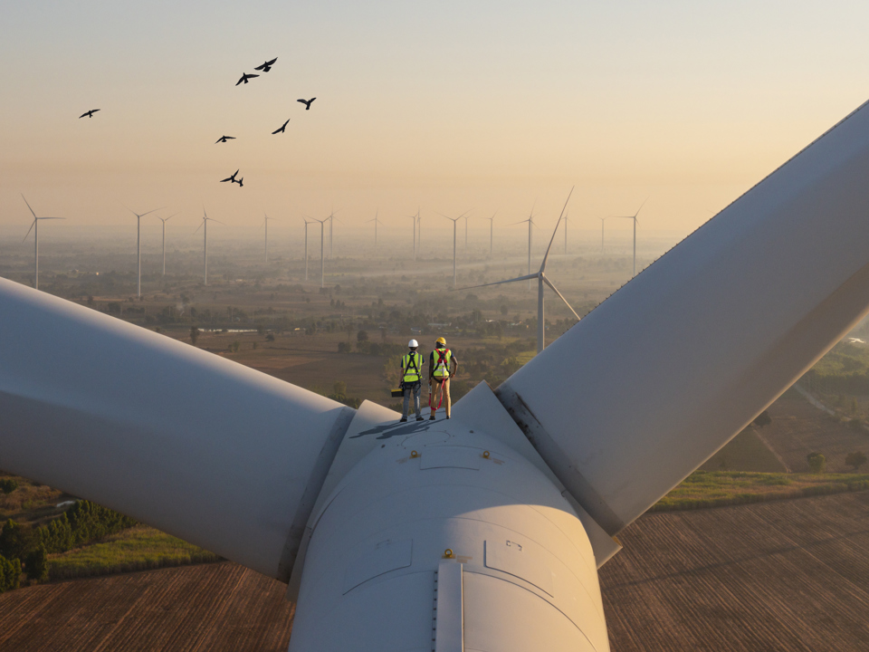 Two workers standing on a wind turbine with panoramic view of the skyline