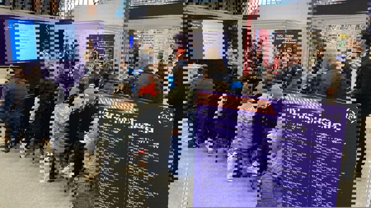 A presenter speaks in front of a screen while a seated audience watches in the IOSH mini‑theatre at a busy conference.