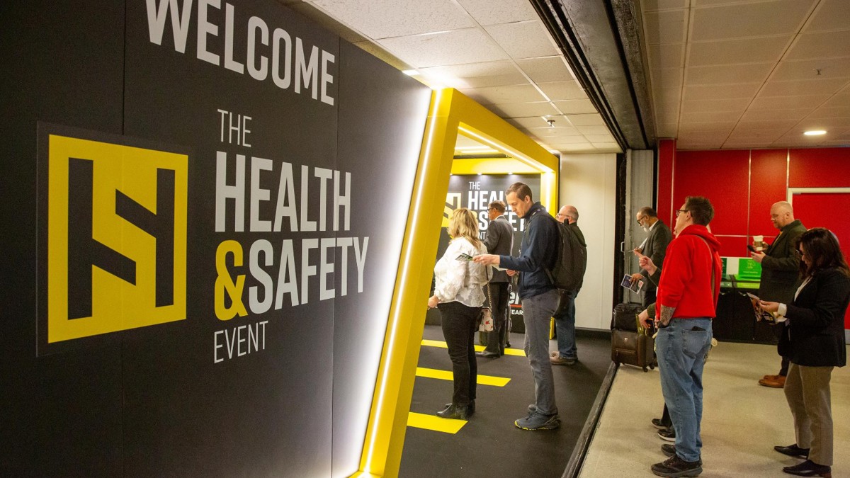 Entrance sign saying: Welcome to the Health and Safety Event as people queue to get in