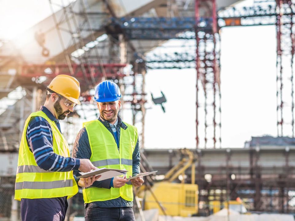 Construction workers in safety gear standing in front of cranes