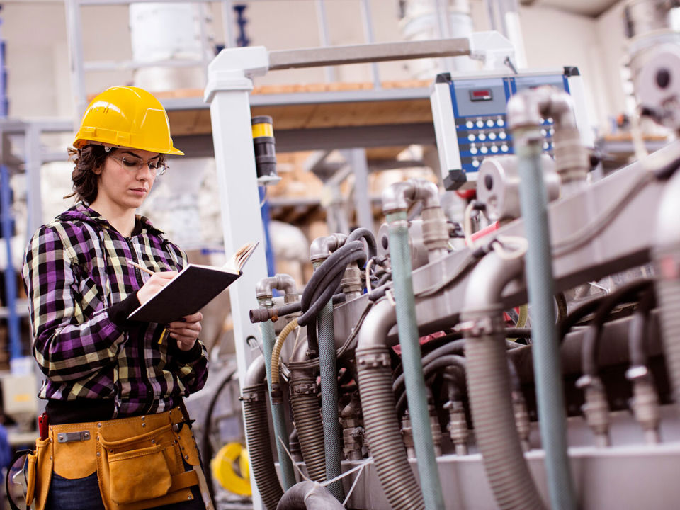Worker in hard hat with clipboard checking equipment in a factory