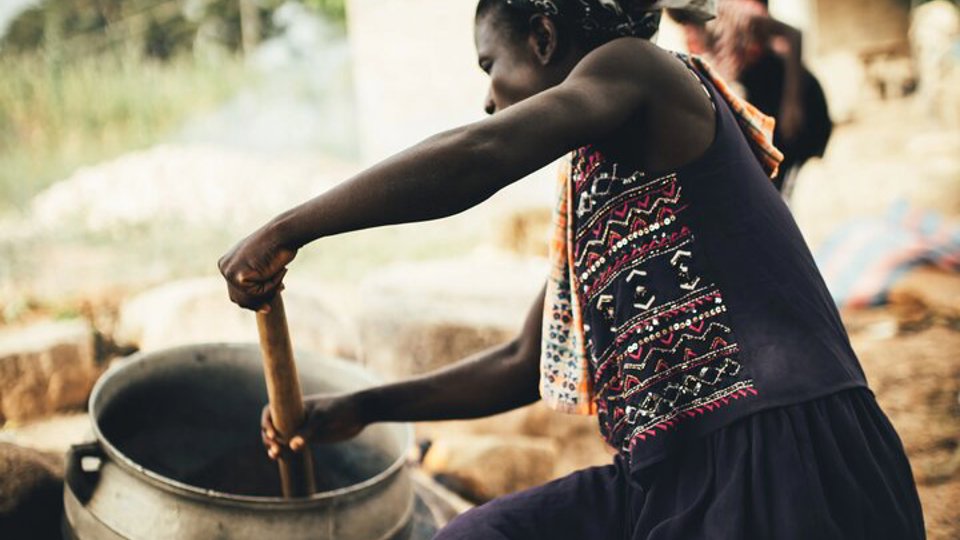 Female worker stirs a pot containing the shea butter mush