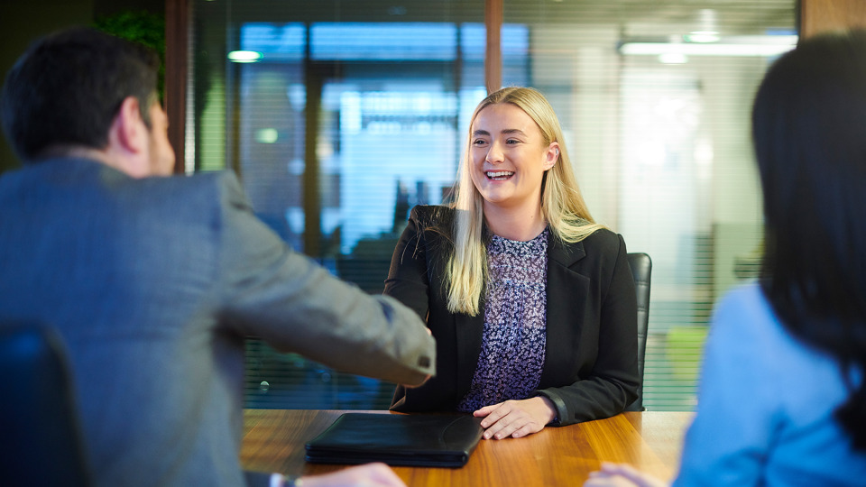 Woman in blazer shakes hands at job interview