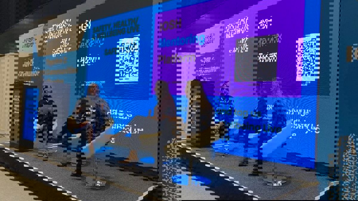 Three panellists sit on stage discussing IOSH mentoring and community topics in front of a large event screen.