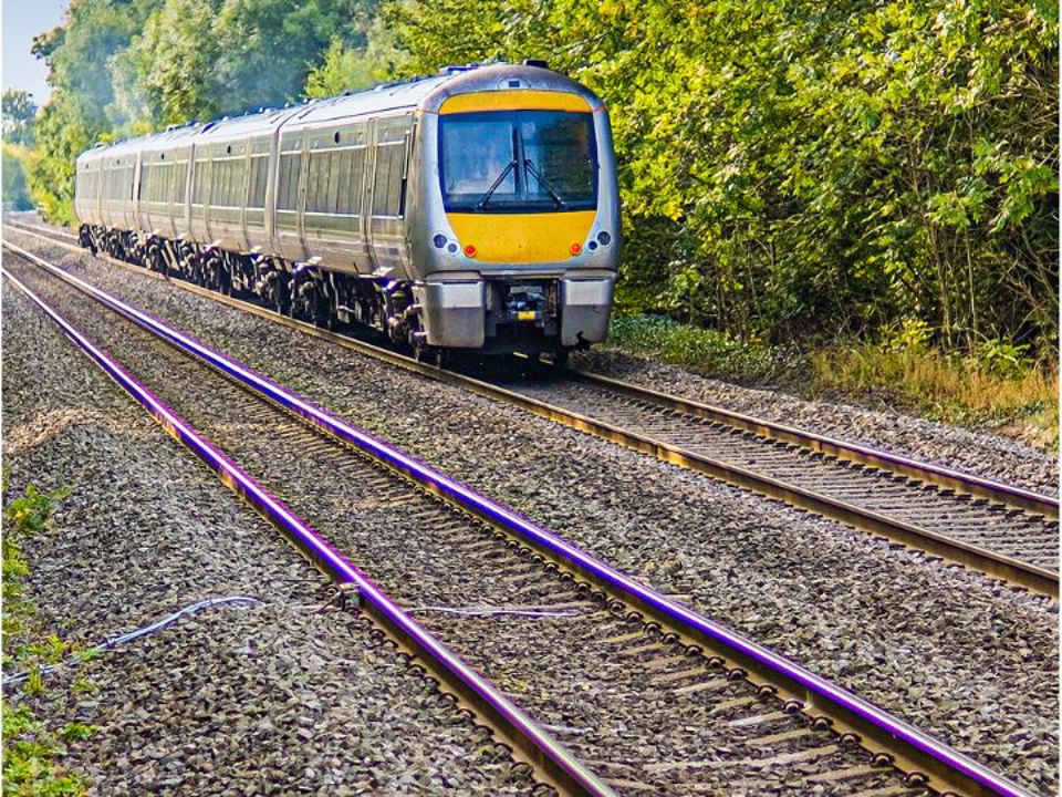 A passenger train travelling along a double‑track railway line surrounded by trees and greenery.
