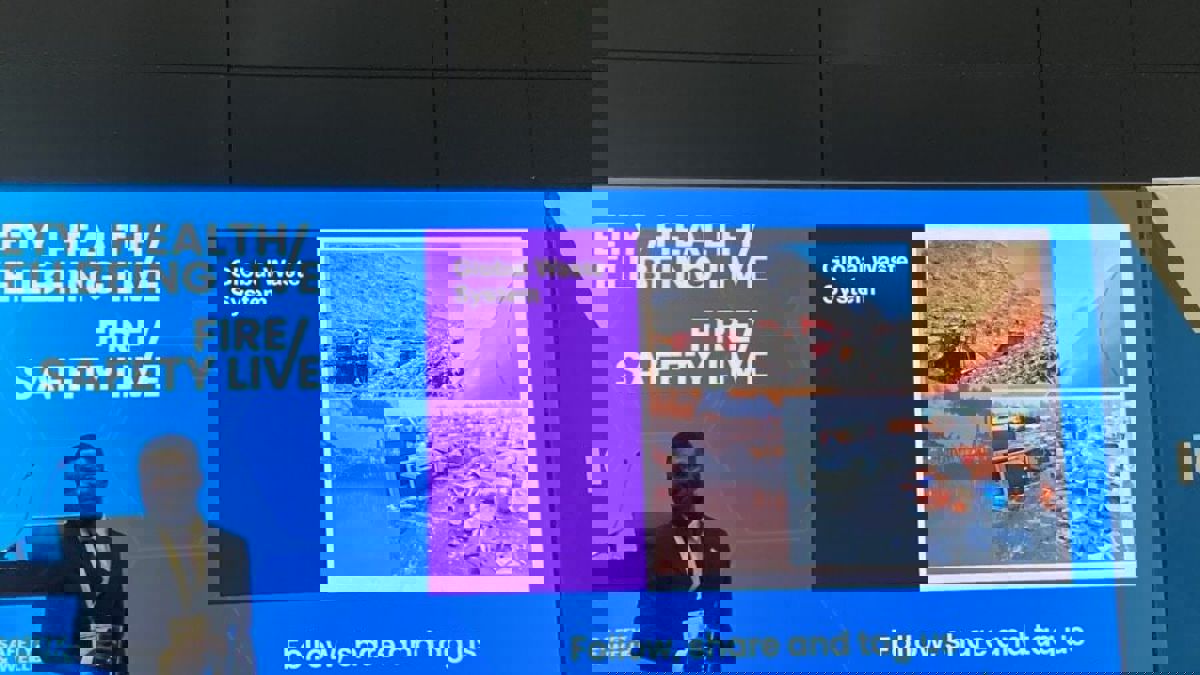 A presenter stands in front of a large screen showing images of global waste sites and the title “Global Waste System”.