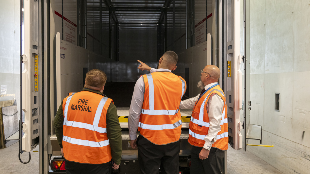 Three workers in high-visibility vests inspecting a loading bay and vehicle interior
