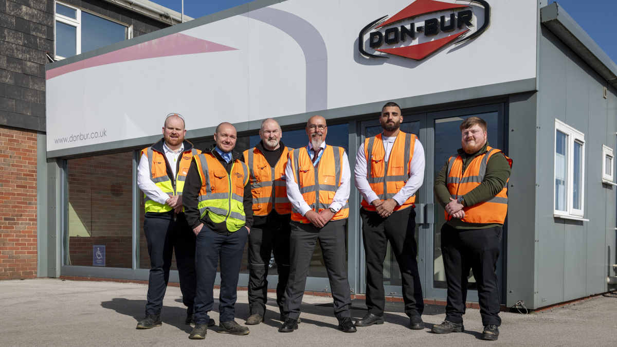 Team in high-visibility vests standing outside workplace building with company signage