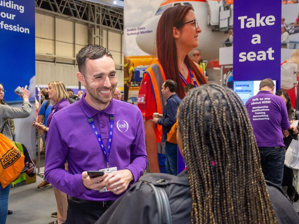 Male IOSH colleague talks to a visitor at our stand at a safety and health show