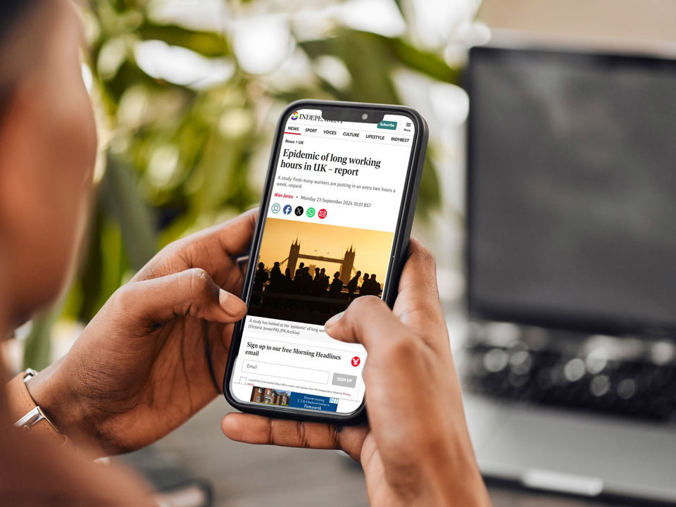 Woman holding phone viewing article about the ‘Epidemic of long working hours’
