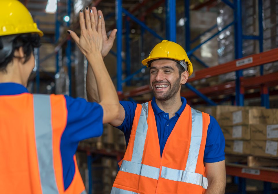 Male worker in hi-vis vest and hard hat high-fiving a colleague