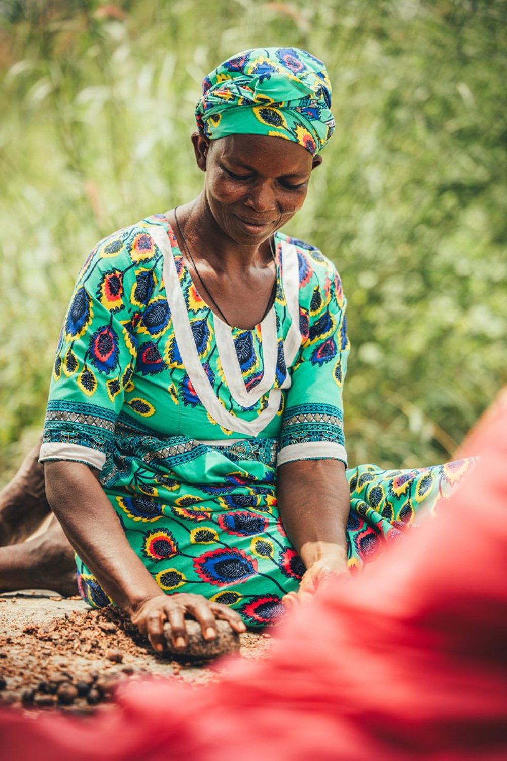 A female worker using a large stone to grind shea butter nuts