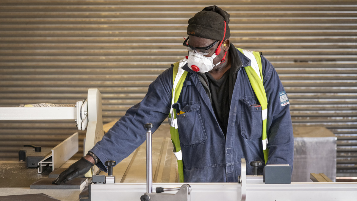 Worker wearing protective mask, goggles and high-visibility vest operating machinery in a workshop